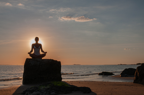 Nainen harjoittelee joogaa istuen kivellä Lootuksessa poseeraamassa auringonlaskun aikaan. Siluetti nainen meditoi rannalla
  - Valokuva, kuva