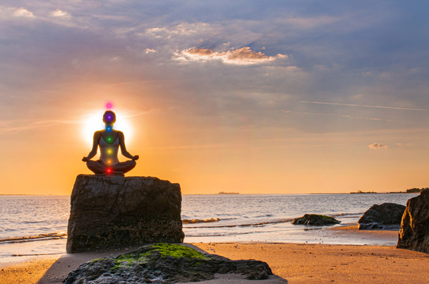 Nainen harjoittelee joogaa istuen kivellä Lootuksessa poseeraamassa auringonlaskun aikaan. Siluetti nainen meditoi rannalla
  - Valokuva, kuva
