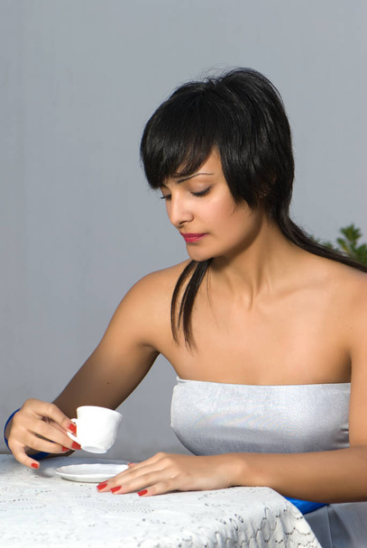 Νεαρή μελαχρινή γυναίκα που πίνει φλιτζάνι καφέ - Φωτογραφία, εικόνα