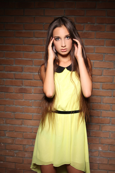 Beautiful young woman posing in yellow dress over brick wall - Fotoğraf, Görsel