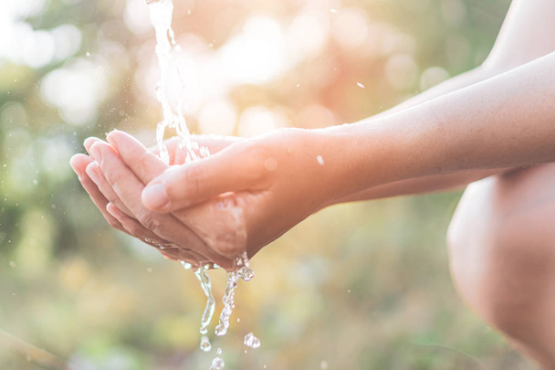 Water from tap to woman hand in nature green park sunset time and bokeh sun light abstract background. - Foto, imagen