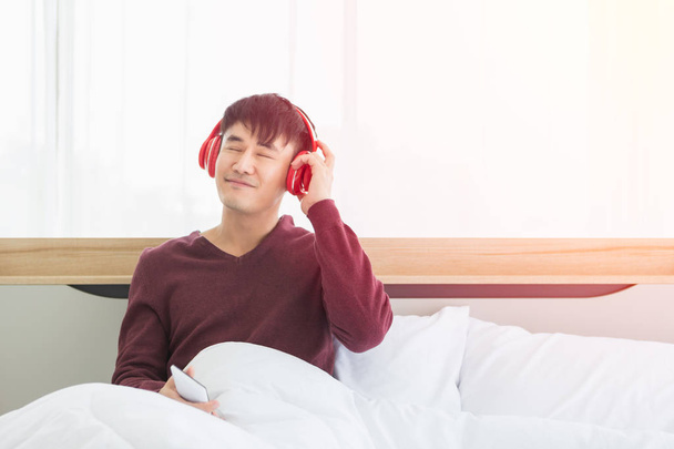 Asian man listen to music by headphone in bedroom - Foto, imagen