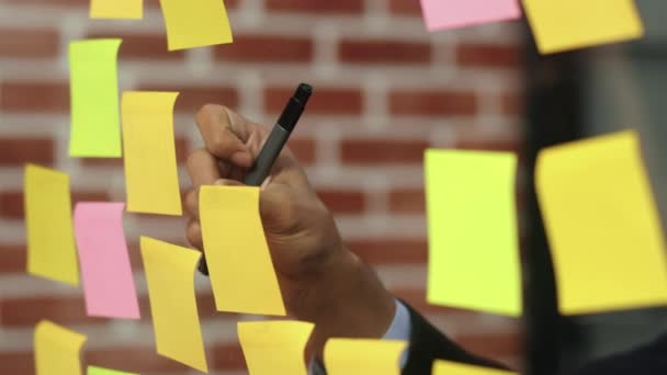 Asian creative man stick a sticky note on glass board. Young professional business male write information, strategy, reminder on paper, business situation, startup in Loft office concept. Slow motion. - Footage, Video