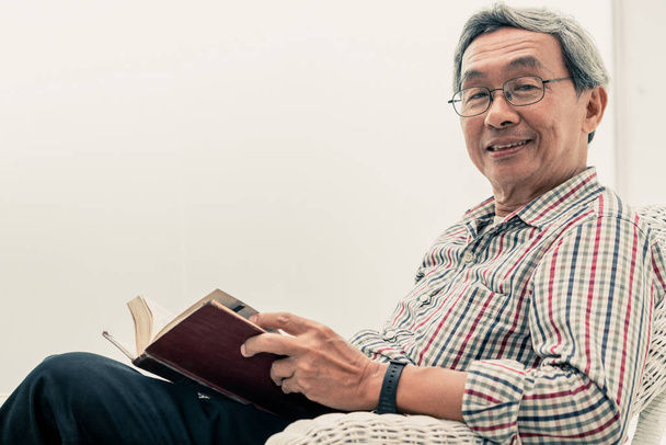 Senior asiatique homme lecture livre sur chaise à la maison
. - Photo, image