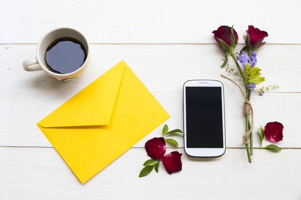 мобільний телефон, гаряча кава еспресо, жовтий конверт і червона троянда розташування плоский стиль на фоні білого дерев'яного
 - Фото, зображення