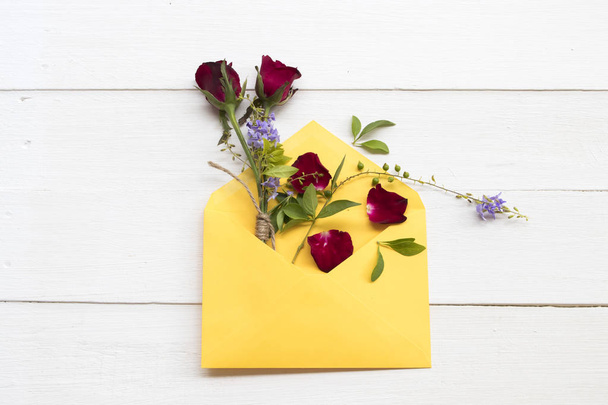 黄色の封筒配置で赤いバラと紫の花は、背景に白い木製のスタイルを平らに敷き葉スタイル - 写真・画像