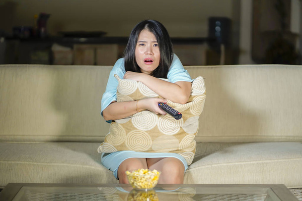 nuori kaunis ja peloissaan Aasian kiinalainen teini nainen pelkää katsomassa kauhu pelottava elokuva kotona sohva syöminen popcorn kulho tilalla kaukosäädin
  - Valokuva, kuva