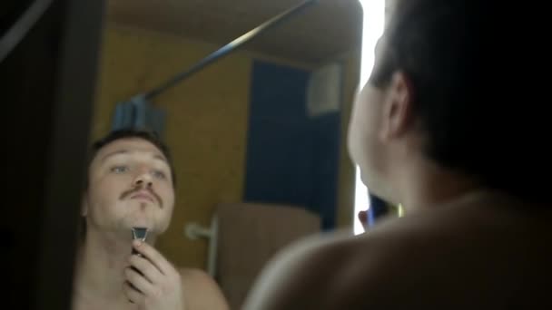 jonge Europese man in een donkere badkamer scheert zijn kin - Video