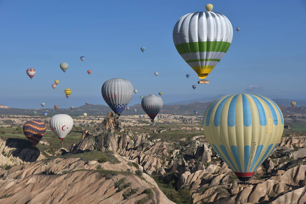 Panoramic view of unusual rocky landscape in Cappadocia, Turkey. Colorful hot air balloons fly in sky over deep canyons, valleys and fairy chimneys of Cappadocia region.  - Fotó, kép