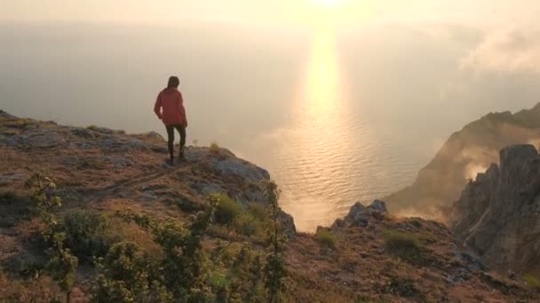 Silhuette van jonge man armen uitgerekt observeren prachtige dramatische kleurrijke zonsondergang boven een zee van een hoge berg in de Krim. - Video
