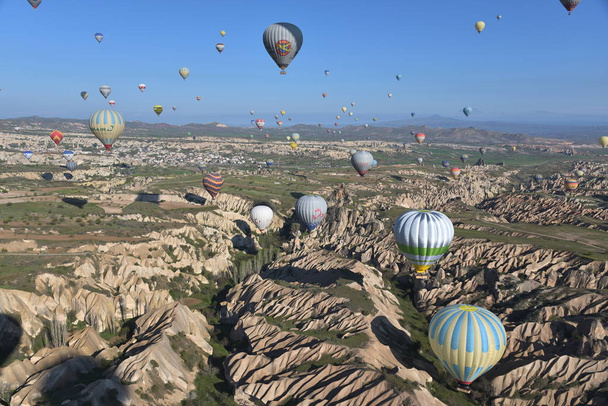Panoramic view of unusual rocky landscape in Cappadocia, Turkey. Colorful hot air balloons fly in sky over deep canyons, valleys and fairy chimneys of Cappadocia region. - Φωτογραφία, εικόνα