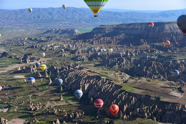 Panoramic view of unusual rocky landscape in Cappadocia, Turkey. Colorful hot air balloons fly in sky over deep canyons, valleys and fairy chimneys of Cappadocia region. - Fotó, kép