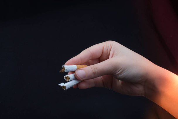 Hand zerbricht eine Zigarette auf schwarzem Hintergrund - Foto, Bild