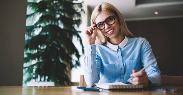 Portrait of happy cheerful hipster girl in eyeglasses looking at camera during preparing information for university course work, positive smiling woman in spectacles learning in college class room - Foto, afbeelding