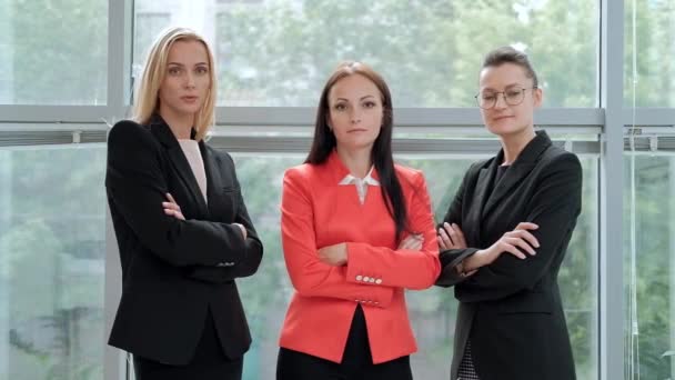 Drie jonge aantrekkelijke vrouwen in business suits poseren tegen de achtergrond van een licht kantoor. Hoofd en ondergeschivelde. Werk team van professionals en collega's. - Video