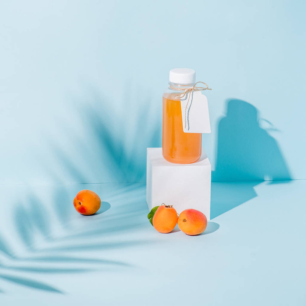 Composition of peach juice on pedestal and fresh apricots, palm branch shadow - Valokuva, kuva