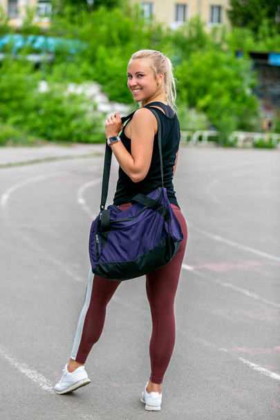 Fitness lifestyle. A thirty-year-old young woman with a sports bag is standing after a workout. Back view. Workout at the stadium. Healthy life concept - Foto, Bild