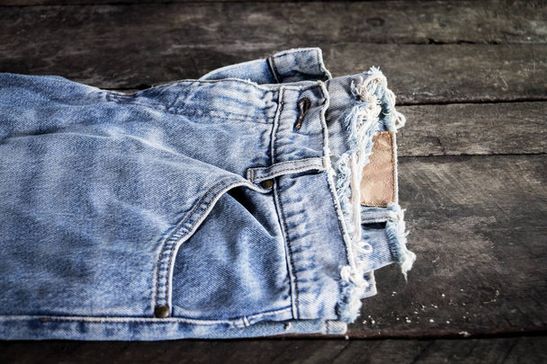 Jeans gestapeld op een houten achtergrond. Blauwe jeans op een bruine houten achtergrond. Gerafeld jeans. Detail van mooie blauwe jeans met lederen riem in vintage stijl. Textuur van blauwe jeans achtergrond - Foto, afbeelding