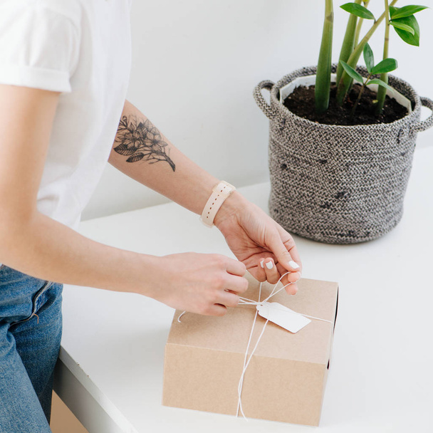 Woman in casual clothes is tying postal cardboard box, attaching tag at home - Photo, Image