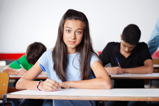 Portrait Of Teenage Schoolgirl Writing At Desk - Foto, imagen