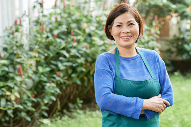 Portrait of senior Vietnamese woman wearing apron when standing in backyard - Foto, Imagen