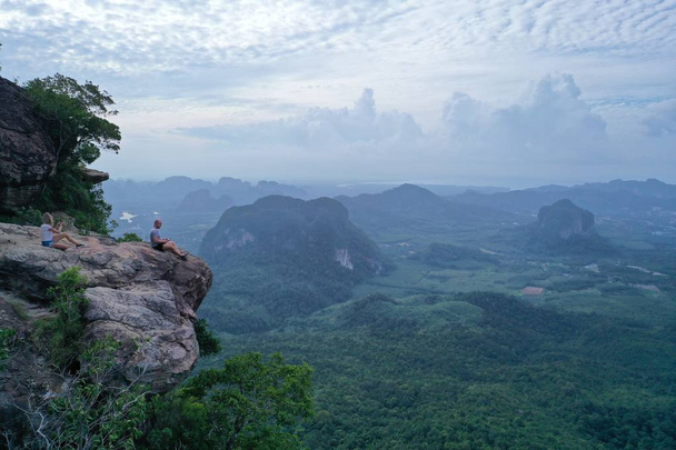 Εναέρια θέα του ζευγαριού στην άκρη του βράχου πάνω από πανέμορφα πράσινα βουνά και φόντο του ουρανού. Άνθρωπος χειριστής κηφήνας και κορίτσι φωτογράφος στο σημείο θέα στο βουνό - Φωτογραφία, εικόνα