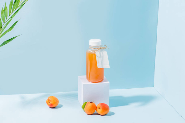 Composition of peach juice on pedestal and fresh apricots, palm branch - Foto, immagini