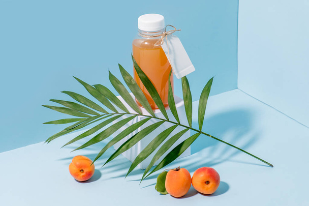 Composition of peach juice on pedestal, fresh apricots and palm branch - Fotoğraf, Görsel