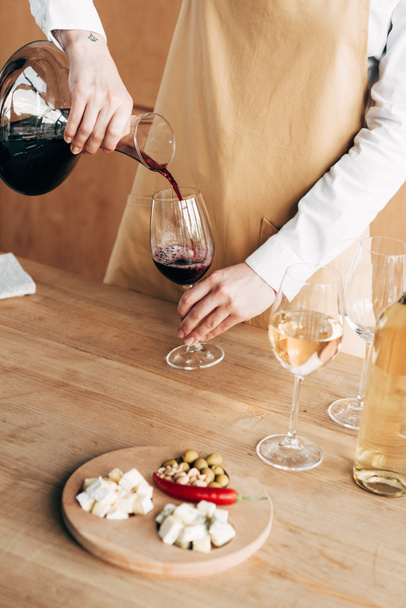vue partielle du sommelier dans un tablier tenant une cruche et versant du vin dans un verre à vin
 - Photo, image