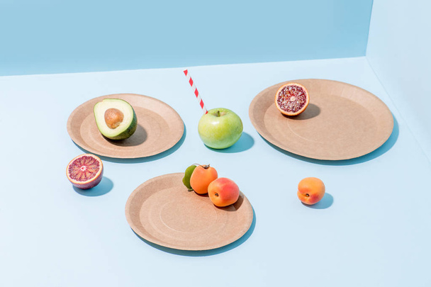 Composition of fruits on compostable paper dishes over blue - Fotografie, Obrázek