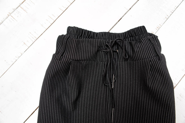 服のファッションコンセプト。白い木製の背景に黒いズボンの詳細。トップビュー - 写真・画像
