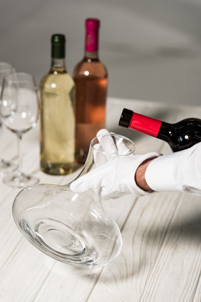 partial view of waiter in white glove pouring wine in jug - Foto, imagen