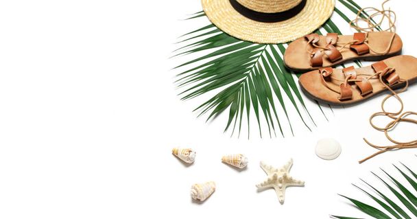 女性のビーチアクセサリーフラットレイ。麦わら帽子、革のサンダル、熱帯ヤシの葉、貝殻、白い背景にヒトデ。トップビューのコピースペース。夏の背景 - 写真・画像