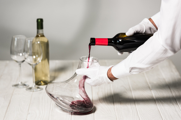 partial view of waiter in white gloves pouring wine in jug - Foto, immagini