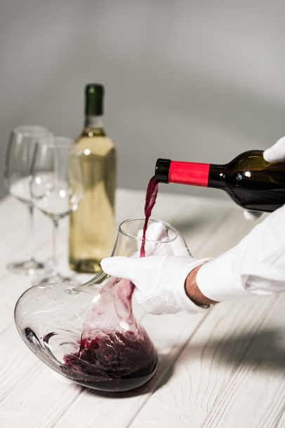 partial view of waiter in white gloves pouring wine in jug - Foto, Bild