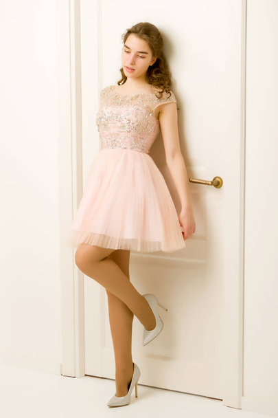 Girl teenager in a smart dress standing near the white door. - Φωτογραφία, εικόνα