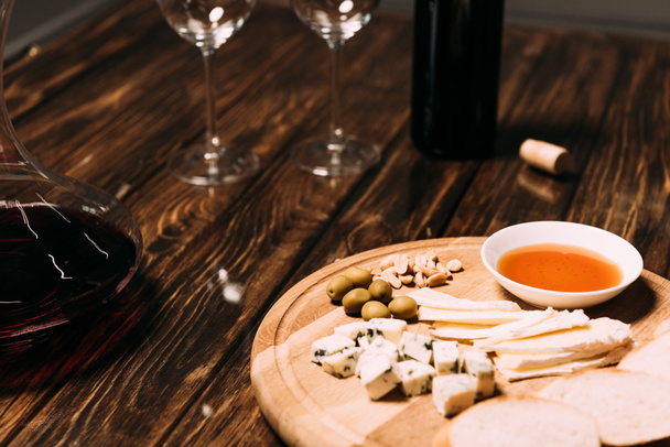 kaas, brood, saus, fles wijn, wijn glazen en kruik op houten oppervlak - Foto, afbeelding