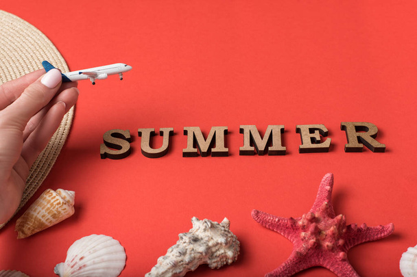 kleines Flugzeug in weiblicher Hand. Wort Sommer aus Holzbuchstaben. Muscheln, Seesterne und lebende Korallen. Urlaubskonzept - Foto, Bild