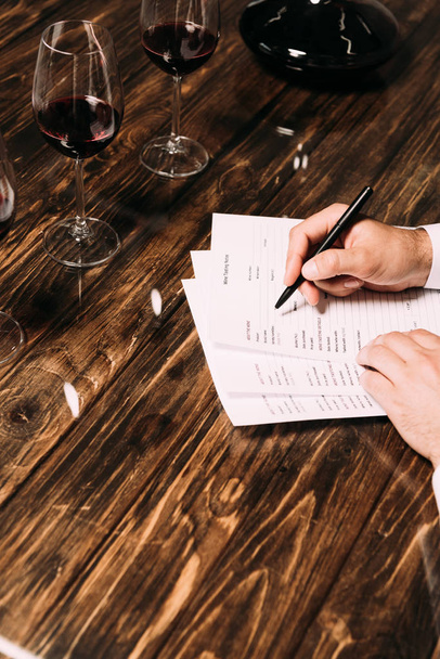 partial view of sommelier writing at table with wine glasses - Foto, Bild