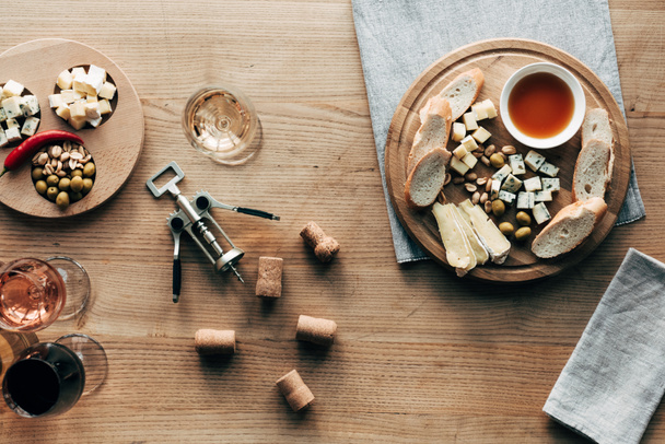 Widok z góry na kieliszki do wina, jedzenie, korkociąg i korki na powierzchni drewnianej - Zdjęcie, obraz