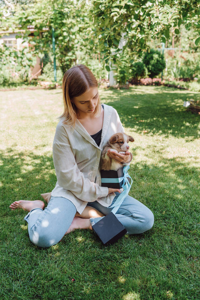 blonde Barefoot meisje zittend in groene tuin met schattige puppy in geschenk doos - Foto, afbeelding