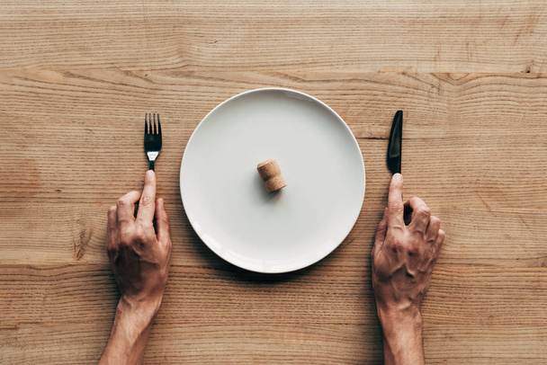 vista ritagliata dell'uomo che tiene forchetta e coltello a tavola con piastra e sughero
 - Foto, immagini