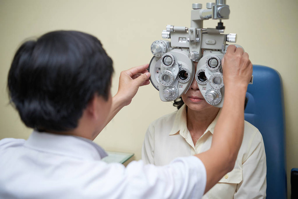 Kypsä nainen katselee fotometrin läpi ja tarkistaa hänen näkönsä silmäklinikalla
 - Valokuva, kuva