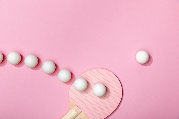 platte lay met witte plastic tafeltennis ballen en racket op roze achtergrond - Foto, afbeelding