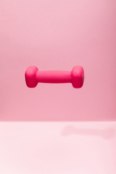 pink bright dumbbell levitating in air on pink background - Fotografie, Obrázek