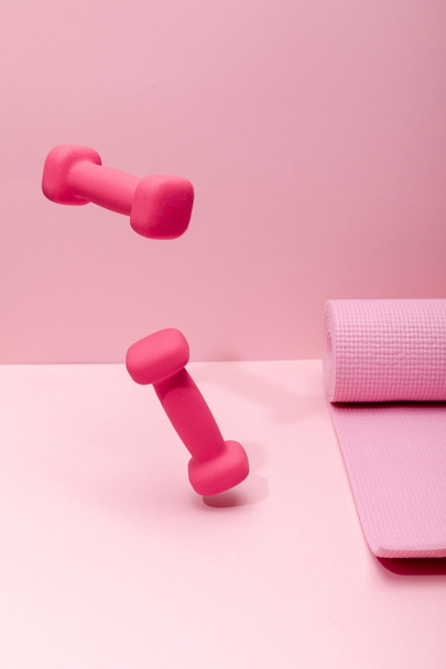pink bright dumbbells levitating in air near rubber fitness mat on pink background - Foto, immagini