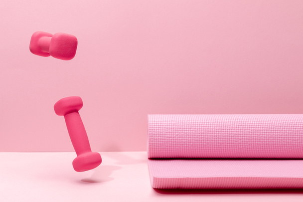 pink bright dumbbells levitating in air near fitness mat on pink background - Fotó, kép
