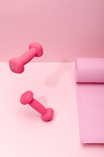 pink bright dumbbells levitating in air near fitness mat on pink background - Photo, Image