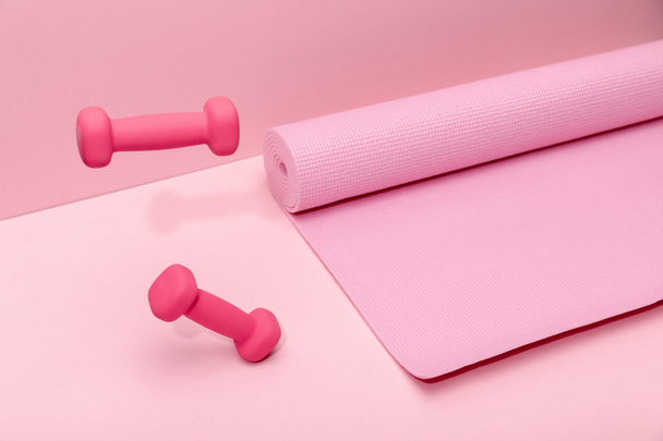 pink bright dumbbells levitating in air near rubber fitness mat on pink background - Фото, изображение