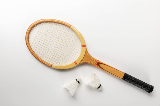 top view of white badminton shuttlecocks scattered near wooden racket on white background - Photo, Image